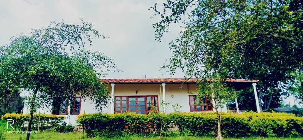 A two-story building with a red-tiled roof, surrounded by lush greenery and trees.