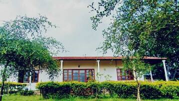A two-story building with a red-tiled roof, surrounded by lush greenery and trees.