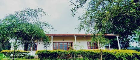 A two-story building with a red-tiled roof, surrounded by lush greenery and trees.