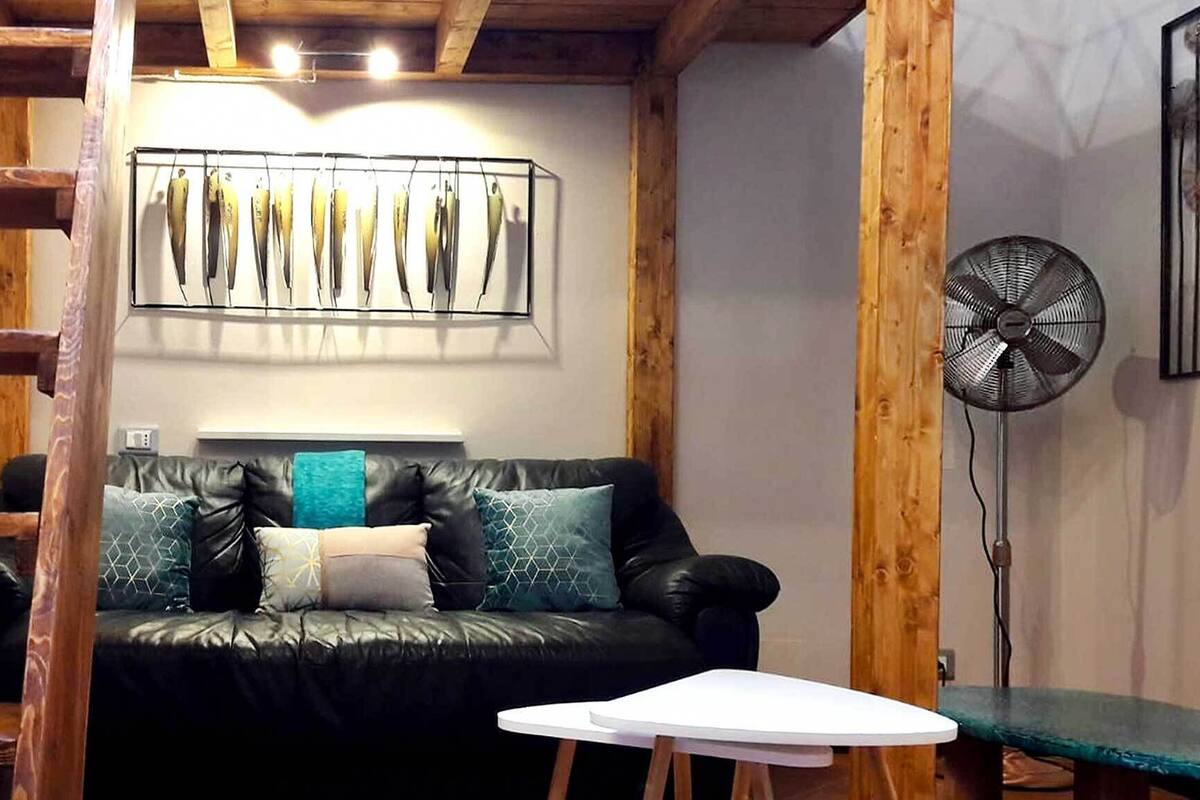 Une pièce chaleureuse avec un canapé en cuir noir, une petite table d’appoint blanche et un plafond en bois.