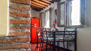 A kitchen with a brick wall, wooden ceiling beams, a red refrigerator, and a dining table with chairs. - RoHouse delle Conserve (Arezzo)