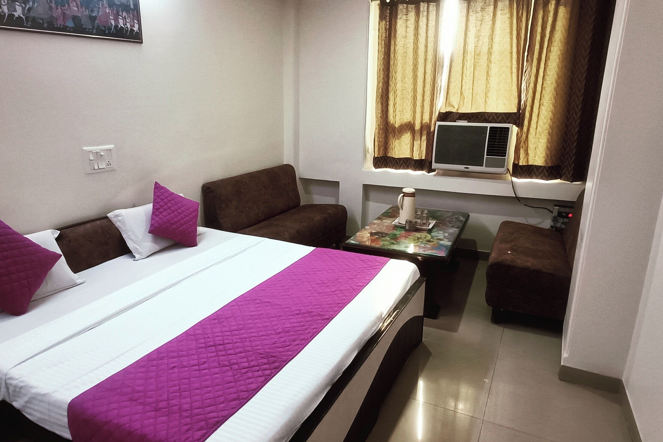 A small, well-lit room with a bed, two sofas, a small table, and a window with curtains.