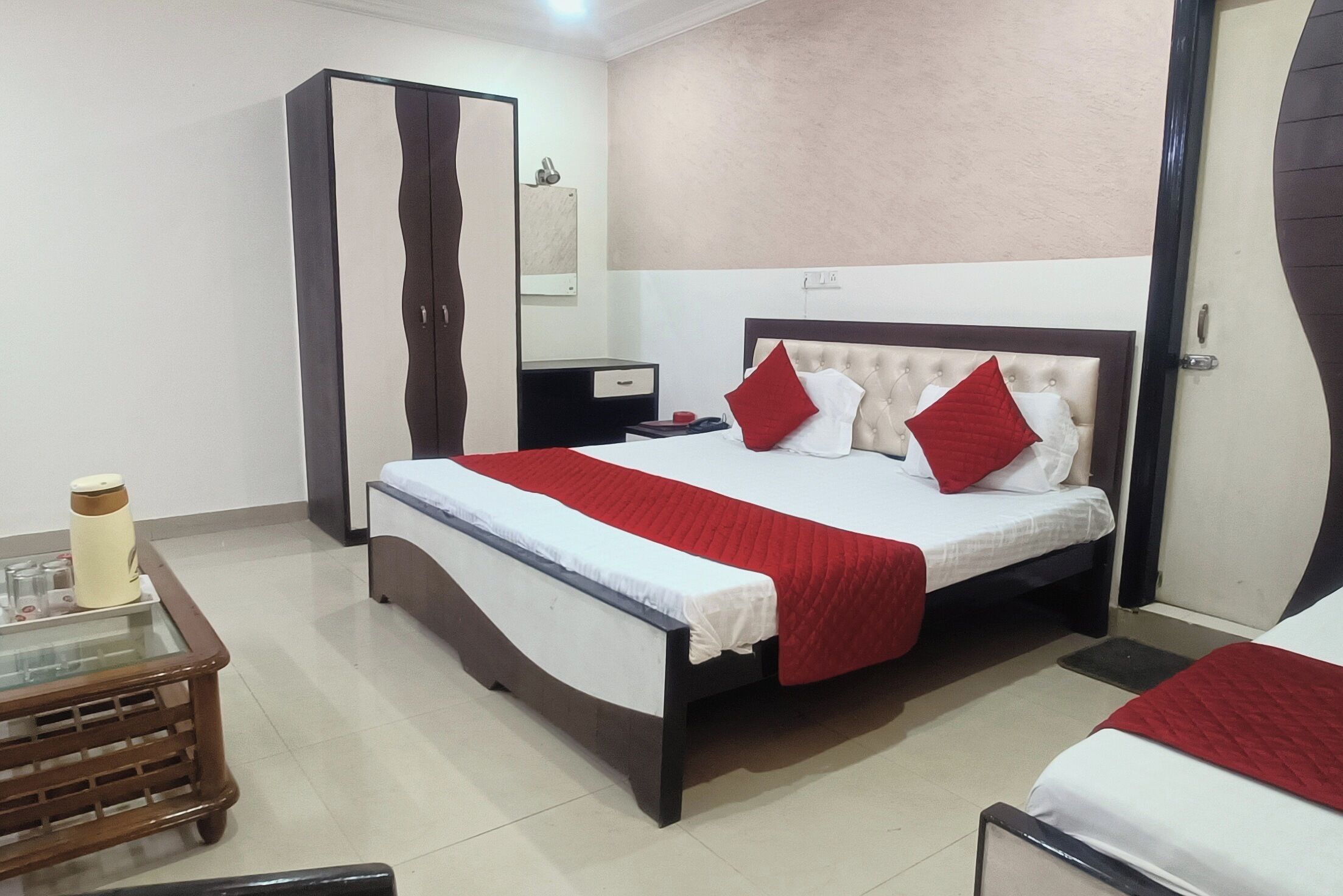 A hotel room with a bed, a wardrobe, a bedside table, and a small table with a thermos.