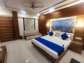 Une chambre avec un grand lit, un canapé, un ventilateur de plafond et un mur décoré d’un aquarium.
