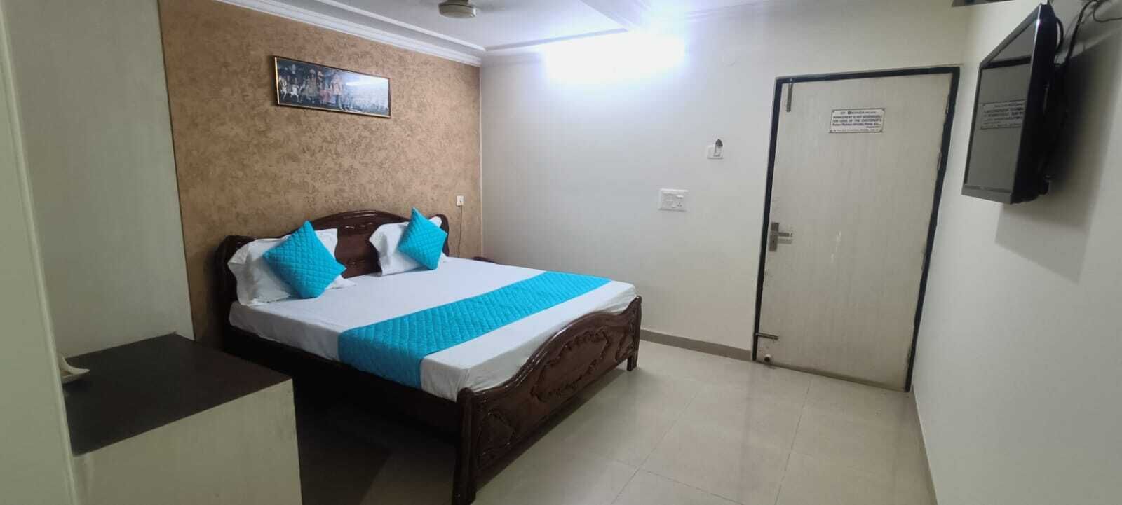 Un dormitorio con cama, una puerta y televisor instalado en la pared.