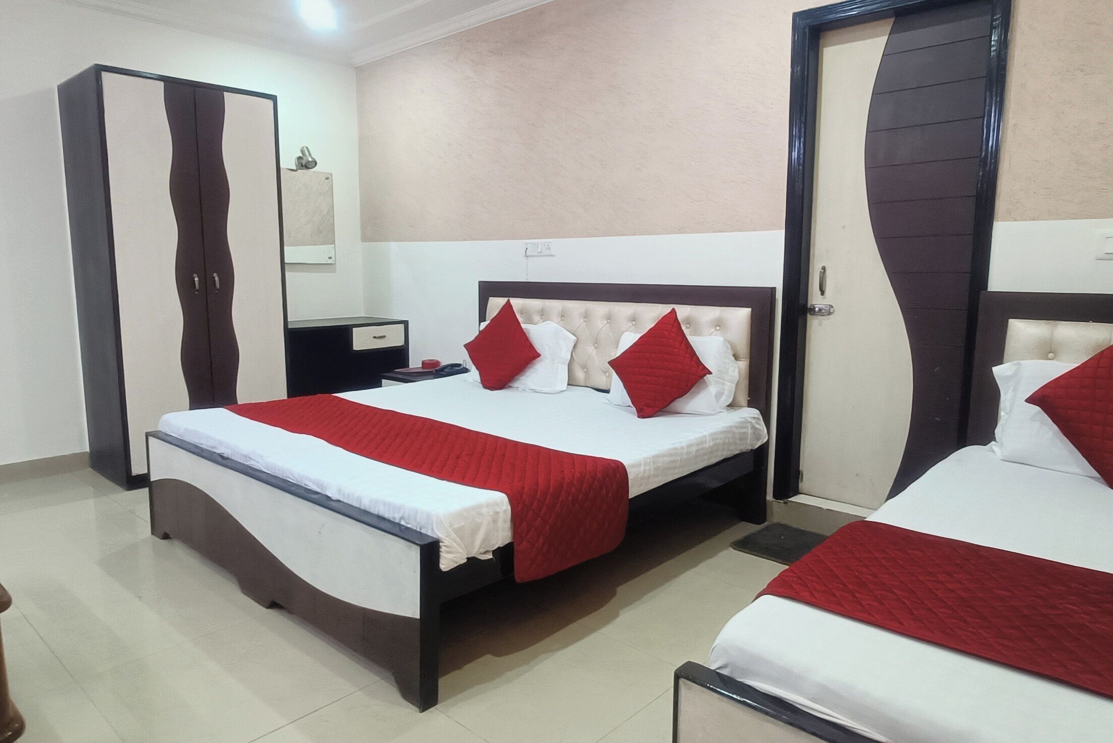 A hotel room with two beds, a wardrobe, a bedside table, and a mirror.