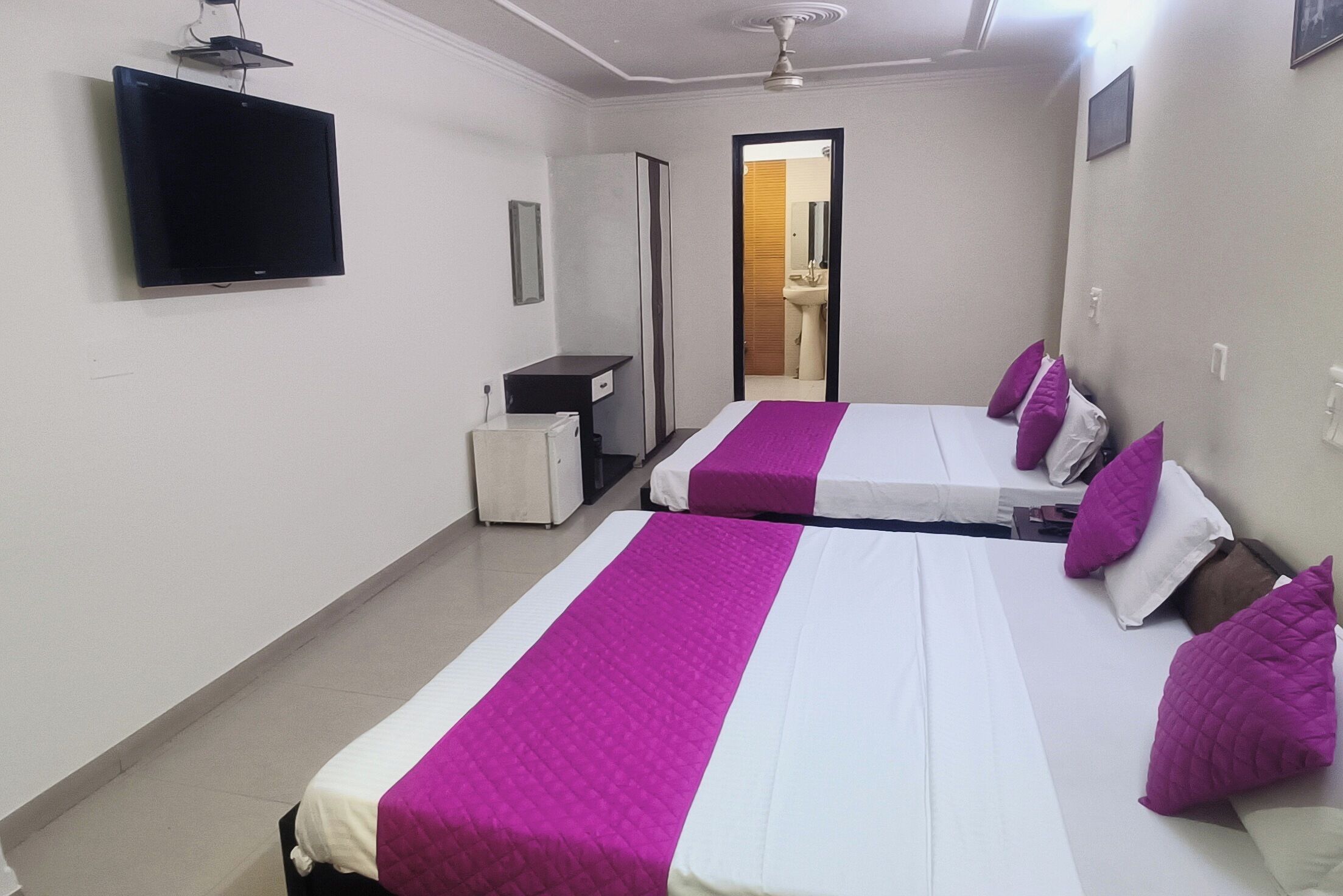 A hotel room with two beds, a flat-screen TV, a wardrobe, and a mirror.