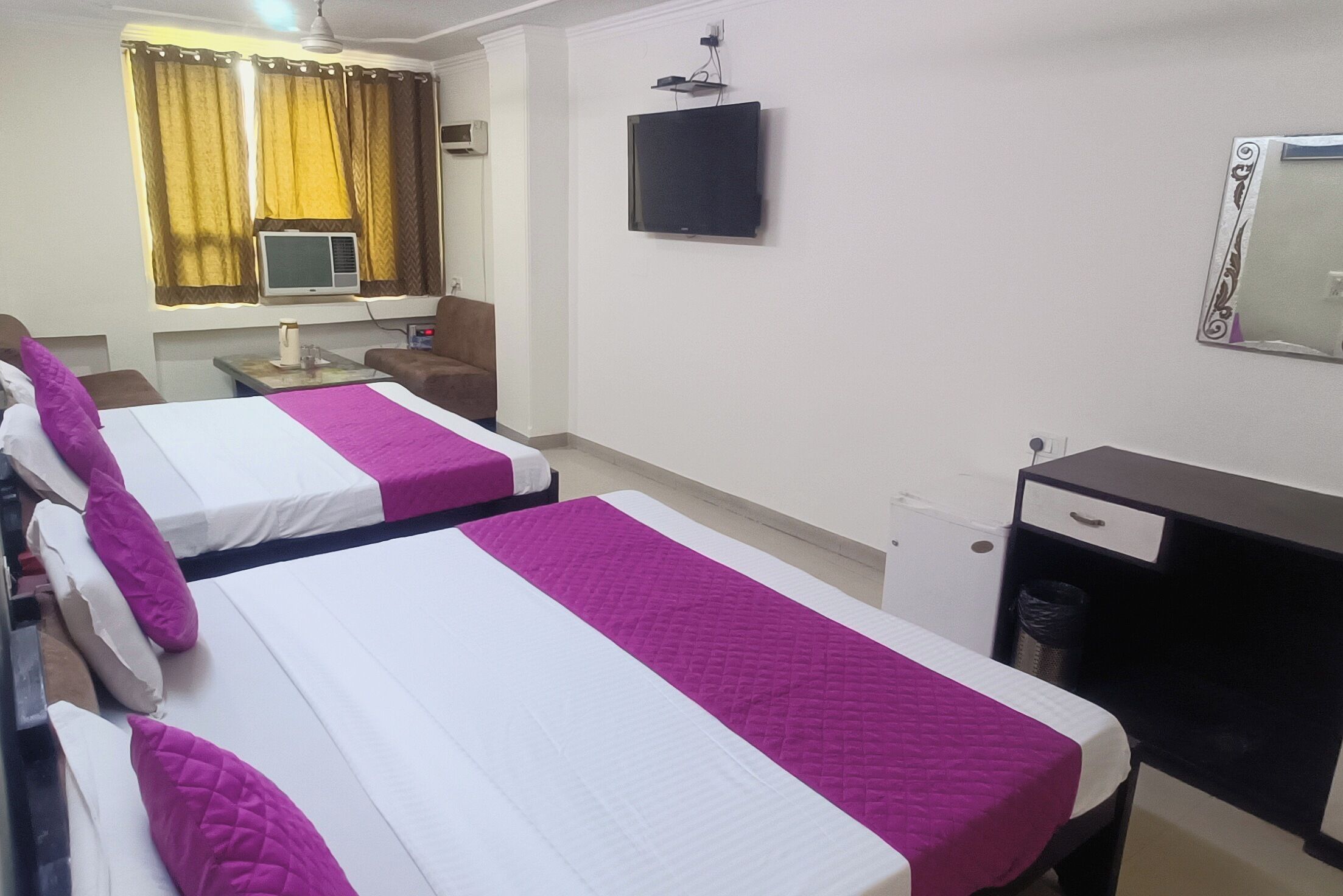 A hotel room with two beds, a desk, a chair, a TV, and a window with curtains.