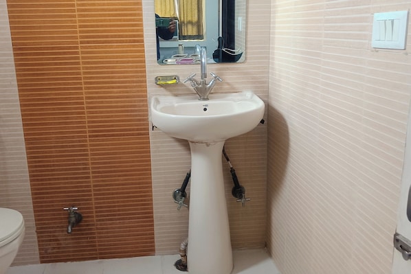 A bathroom with a white pedestal sink, a mirror above it, and a toilet to the left.