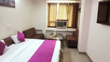 A hotel room with a bed, a sofa, a small table, and a television.