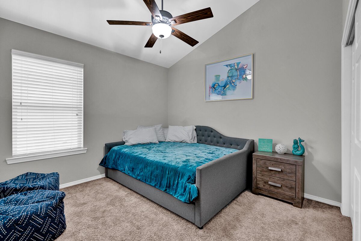 A bedroom with a bed, a ceiling fan, a nightstand, a chair, and a window with blinds.