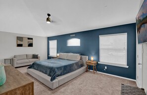 Une chambre à coucher avec un lit, une table de chevet, une lampe, une fenêtre et un ventilateur de plafond.