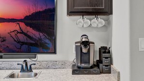 Cucina con mobili in legno scuro, un piano di lavoro in granito, una macchina da caffè e un grande quadro incorniciato raffigurante un tramonto su un lago.