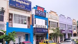 Vista da rua com um hotel chamado 'Al-Baghdadi' e 'SNO HOTEL', com placas visíveis.