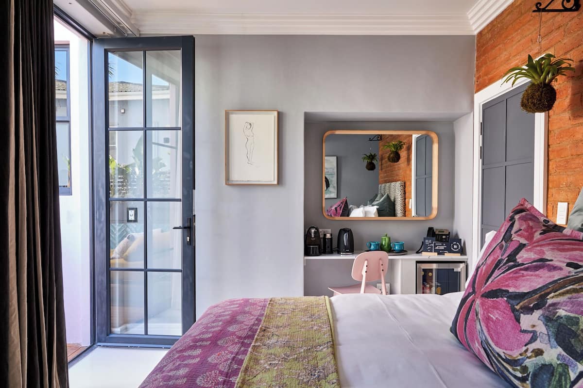 A bedroom with a bed, a desk, a chair, a mirror, and a door.