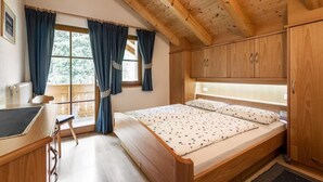 Un dormitorio acogedor con una cama de madera, un escritorio y una silla, con un ventanal con cortinas.