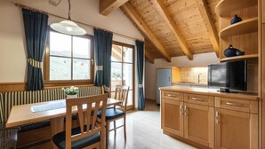 Una cocina acogedora con armarios de madera, una mesa de comedor con sillas, un televisor y una ventana con cortinas.