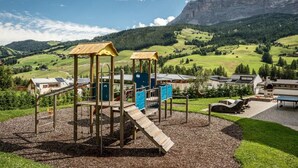 Un parque infantil con estructuras para escalar y toboganes, con vistas a un paisaje montañoso y edificios residenciales.