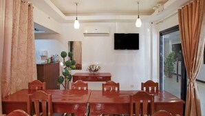 A dining area with a wooden table and chairs, a flat-screen TV mounted on the wall, and a potted plant on the table. - OYO 459 Offshore Hotel (General Santos)
