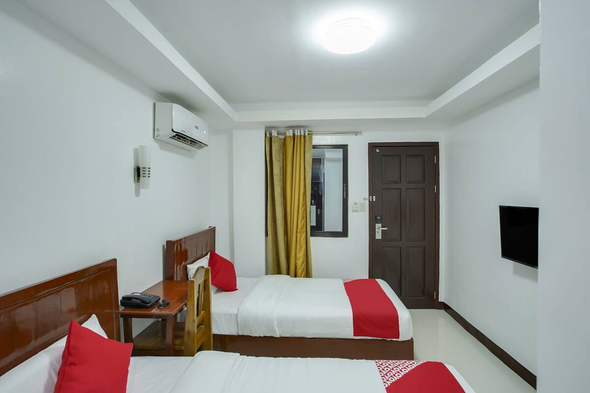 Quarto de hotel com duas camas, uma escrivaninha com telefone, ar condicionado, televisão e uma porta.
