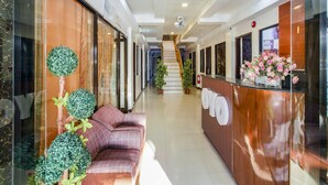 A hotel reception area with a reception desk, a staircase, and a seating area with a couch and potted plants. - OYO 459 Offshore Hotel (General Santos)