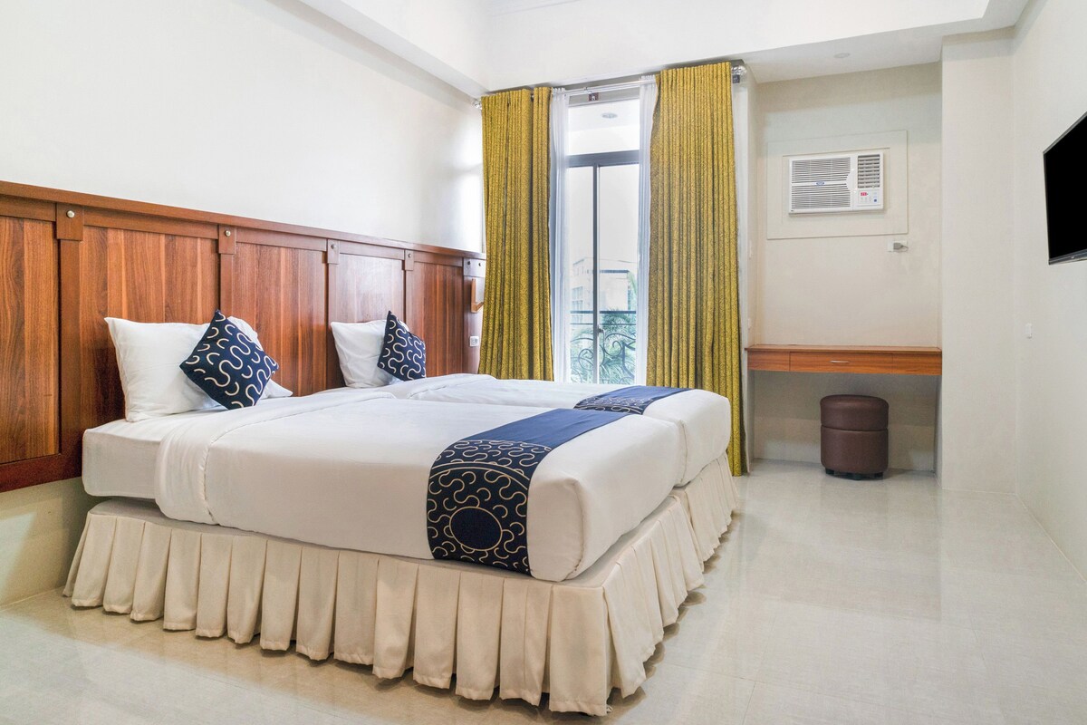 Camera d'albergo con un letto grande, testiera in legno e vista sull'esterno attraverso una finestra con tende gialle.