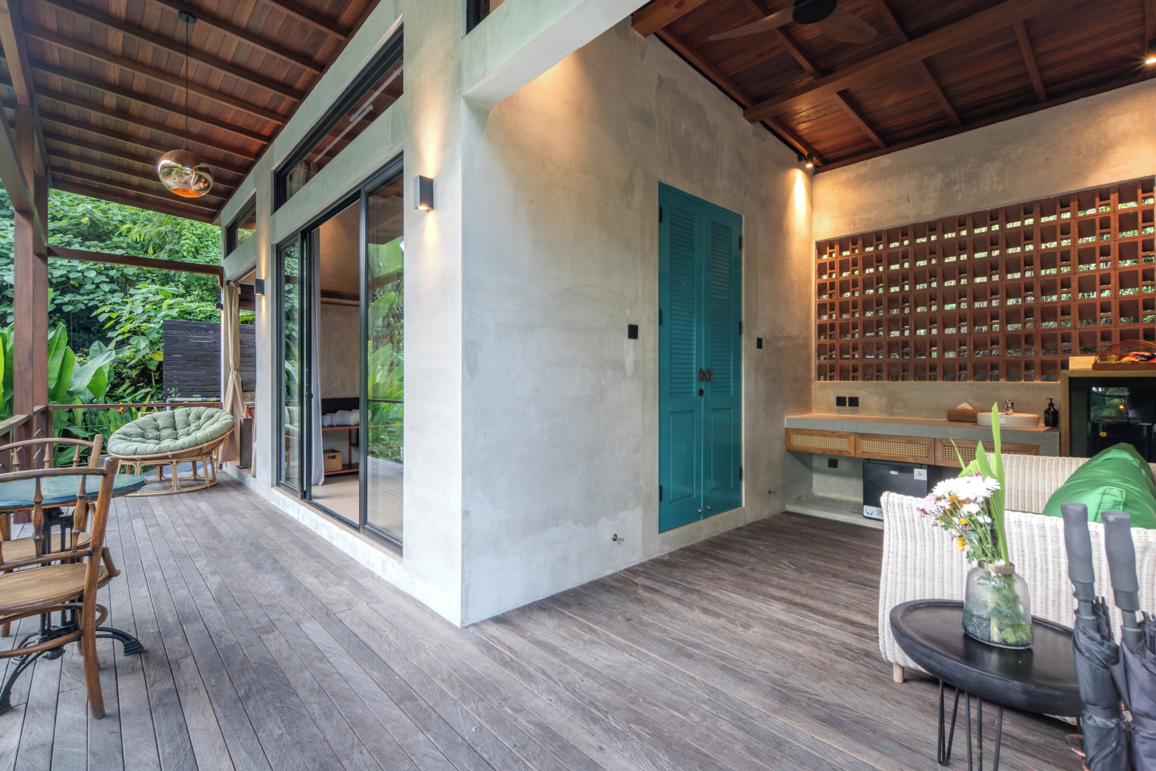 Un interior moderno con terraza de madera, zona de comedor con sillas, cocina con estanterías empotradas y un amplio ventanal corredero.