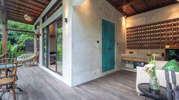 Un interior moderno con terraza de madera, zona de comedor con sillas, cocina con estanterías empotradas y un amplio ventanal corredero.