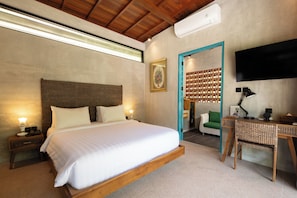 A bedroom with a large bed, bedside tables, a desk, a chair, a television, and a door leading to another room. - Kadewa Retreat Ubud - Adults Only (Ubud)