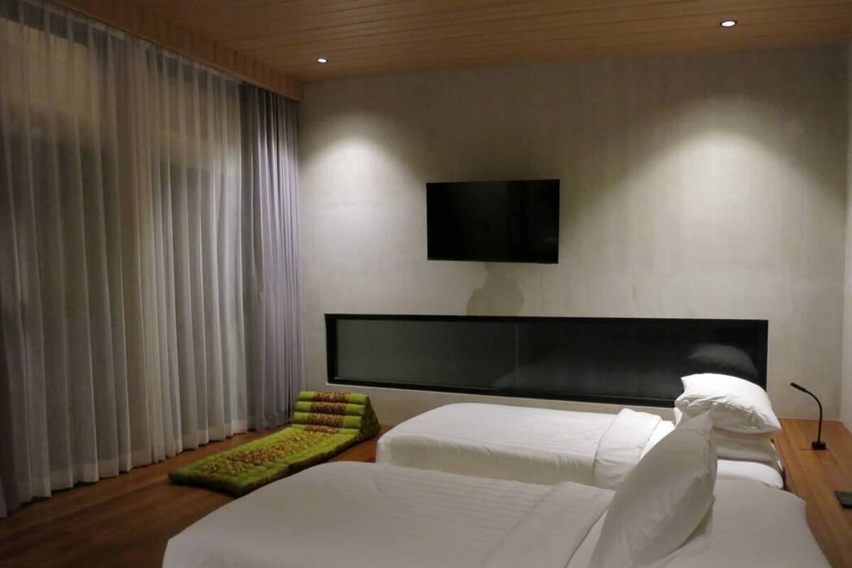 A modern hotel room with a large bed, a flat-screen TV mounted on the wall, and a wooden ceiling.
