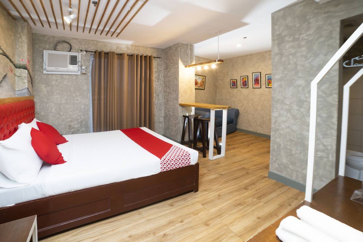 A modern hotel room with a wooden bed, a desk, and a dining area.