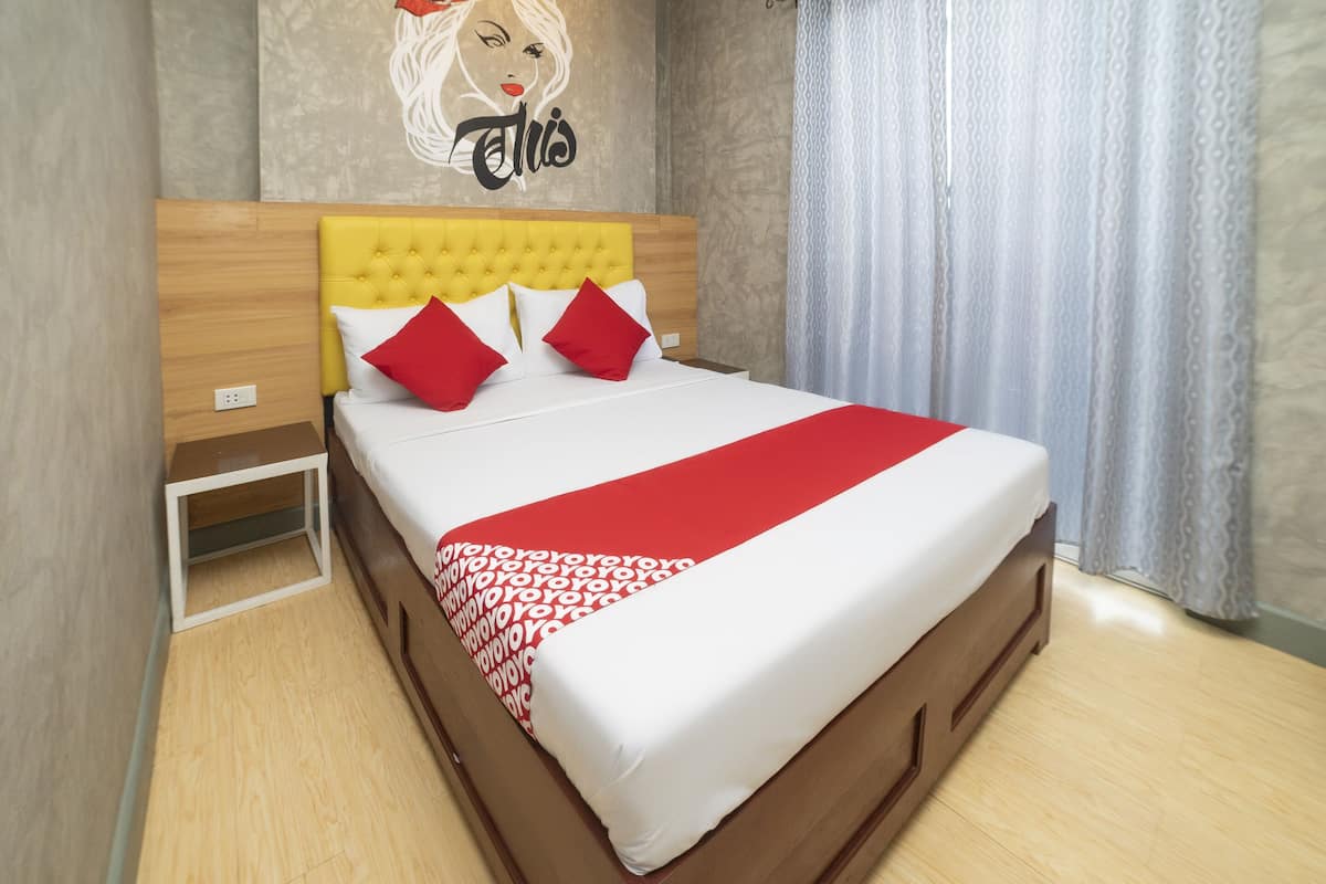 A neatly made bed with a red and white bedspread, a yellow tufted headboard, and two red pillows.