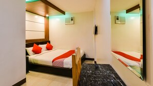 A hotel room with a bed, a wooden headboard, a red and white patterned throw, and a marble floor.