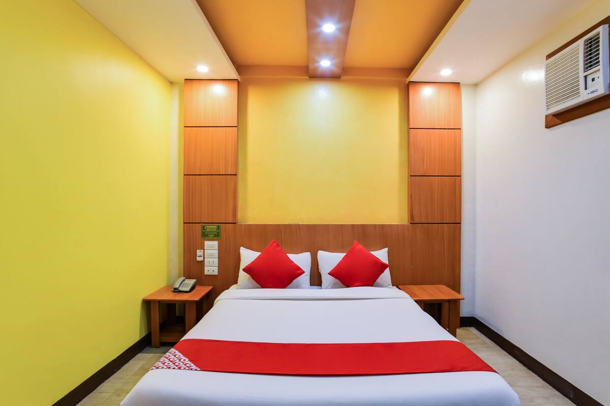 Ein Hotelzimmer mit einem Bett, zwei Nachttischen, einem Telefon und einer wandmontierten Klimaanlage.