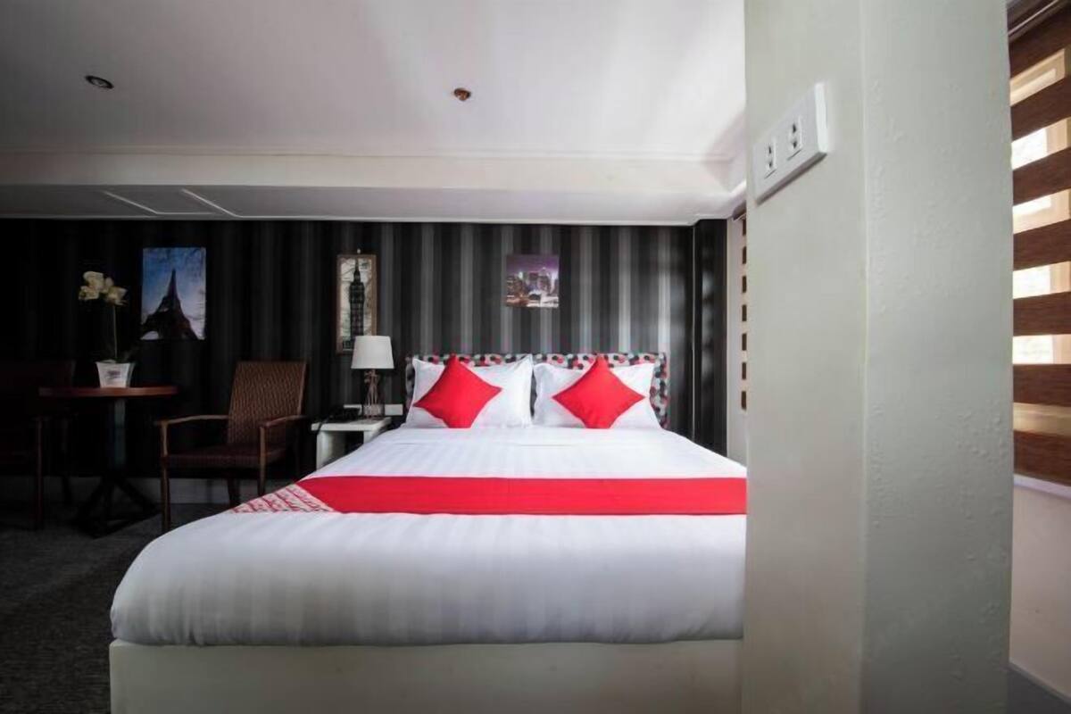 Ein Hotelzimmer mit einem Bett, einem Schreibtisch, einem Stuhl und einem kleinen Tisch mit einer Lampe.