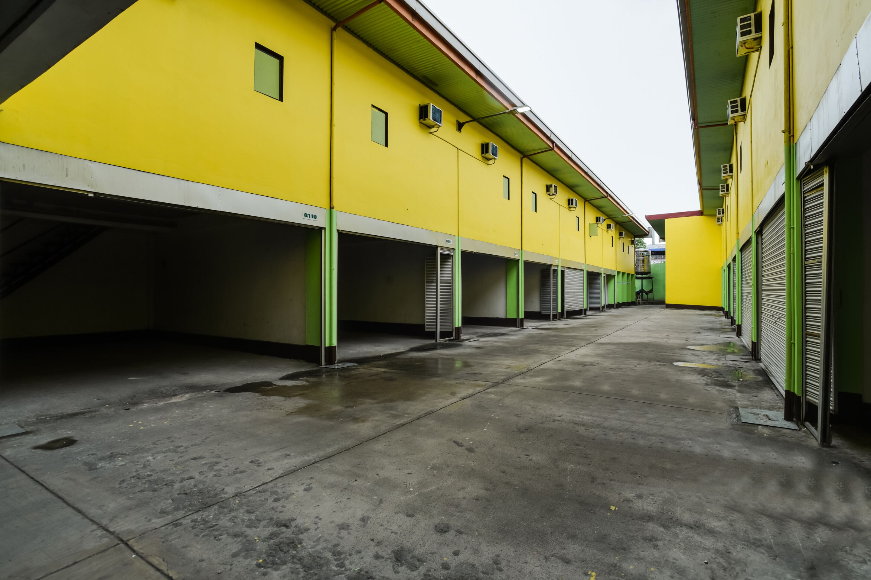 A long, narrow corridor with multiple green-framed doors, likely leading to parking spaces or storage areas, in a building with yellow walls.