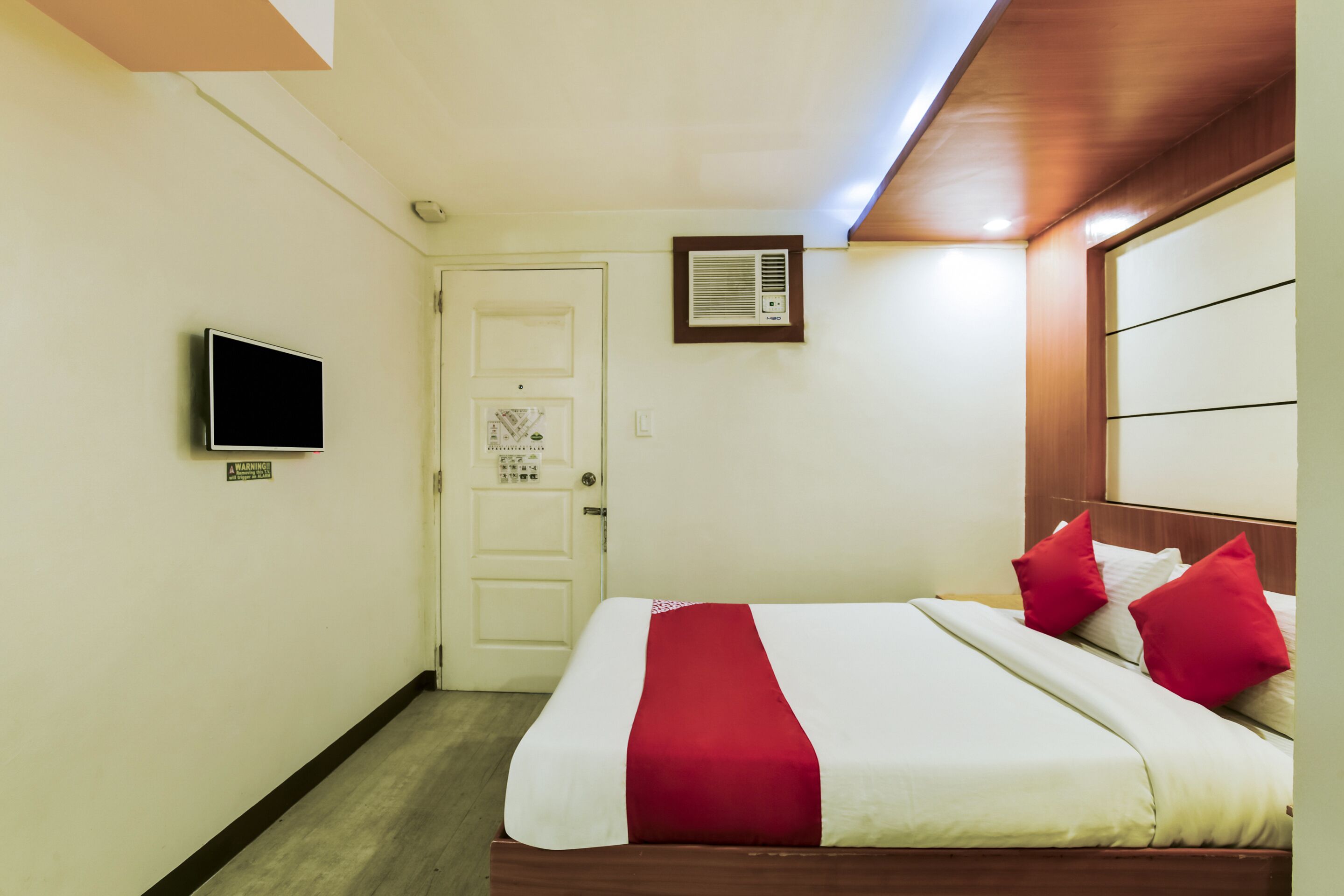 Una habitación de hotel con una cama, televisor, puerta y aire acondicionado.