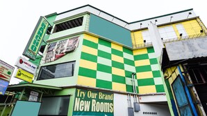 A multi-story building with a green and yellow checkered facade, a sign advertising 'Try Our Brand New Rooms', and an entrance marked 'Drive-In'.