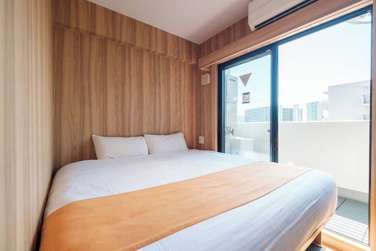 Ein modernes Hotelzimmer mit einem großen Bett, Holzvertäfelung an den Wänden und einem Balkon mit Blick auf die Stadt.