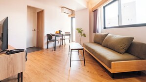 A modern living room with a sofa, a small table, and a TV on a wooden desk. - HomeNest Hotel Tennoji (Osaka)
