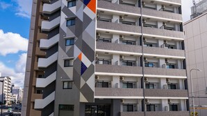 A multi-story building with a modern design, featuring a prominent logo on the facade. - HomeNest Hotel Tennoji (Osaka)