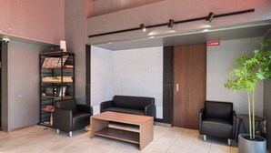 A modern lobby with a wooden coffee table, two black sofas, a bookshelf, and a potted plant. - HomeNest Hotel Tennoji (Osaka)