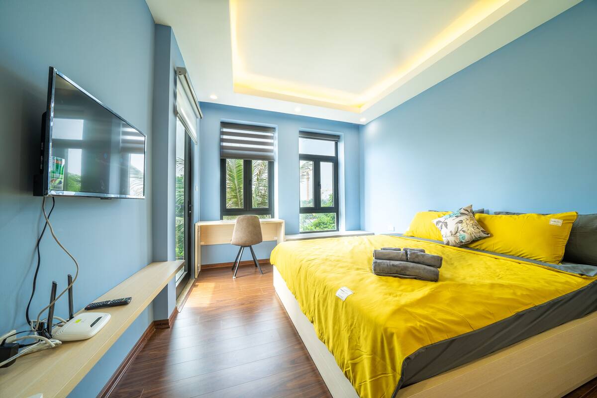 A modern bedroom with a large bed, a desk, and a TV.