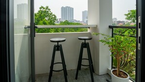 Un balcon avec deux tabourets noirs, une plante en pot et une vue sur les immeubles de la ville.