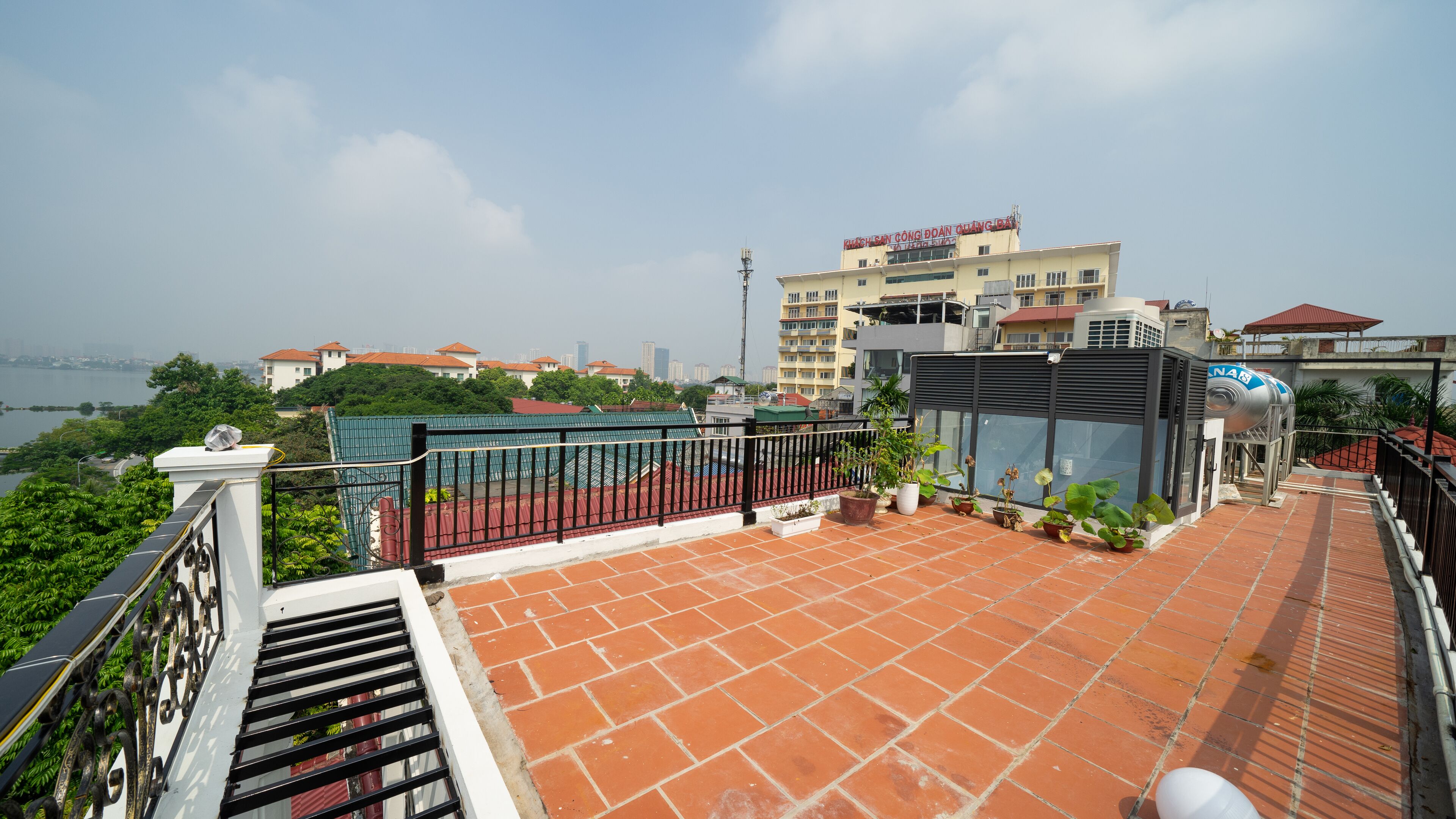 A rooftop terrace with a view of a city skyline, a water body, and a building with a sign in Vietnamese.