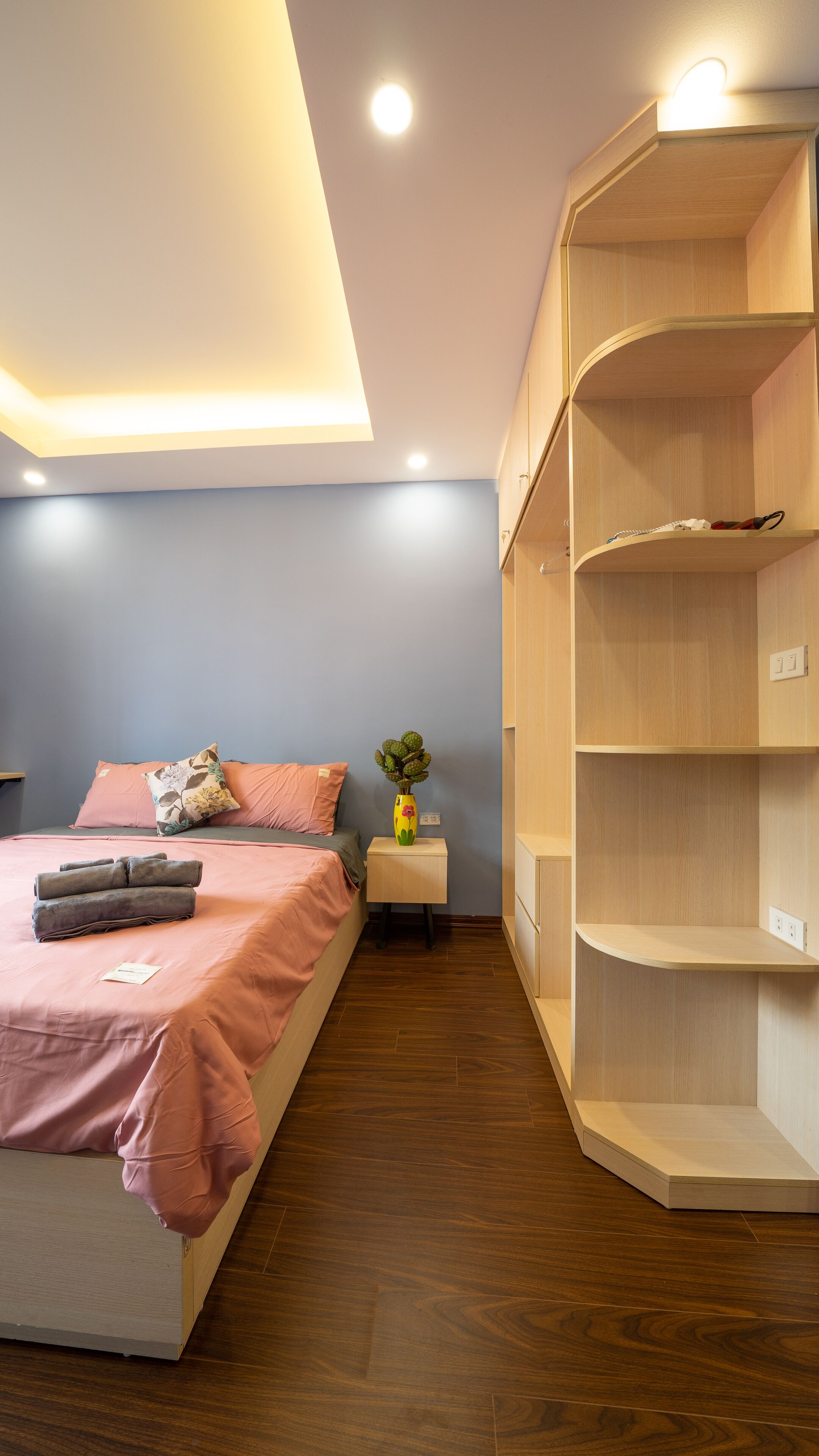 Un dormitorio con una cama, una mesita de noche, una estantería de madera y una lámpara en el techo.