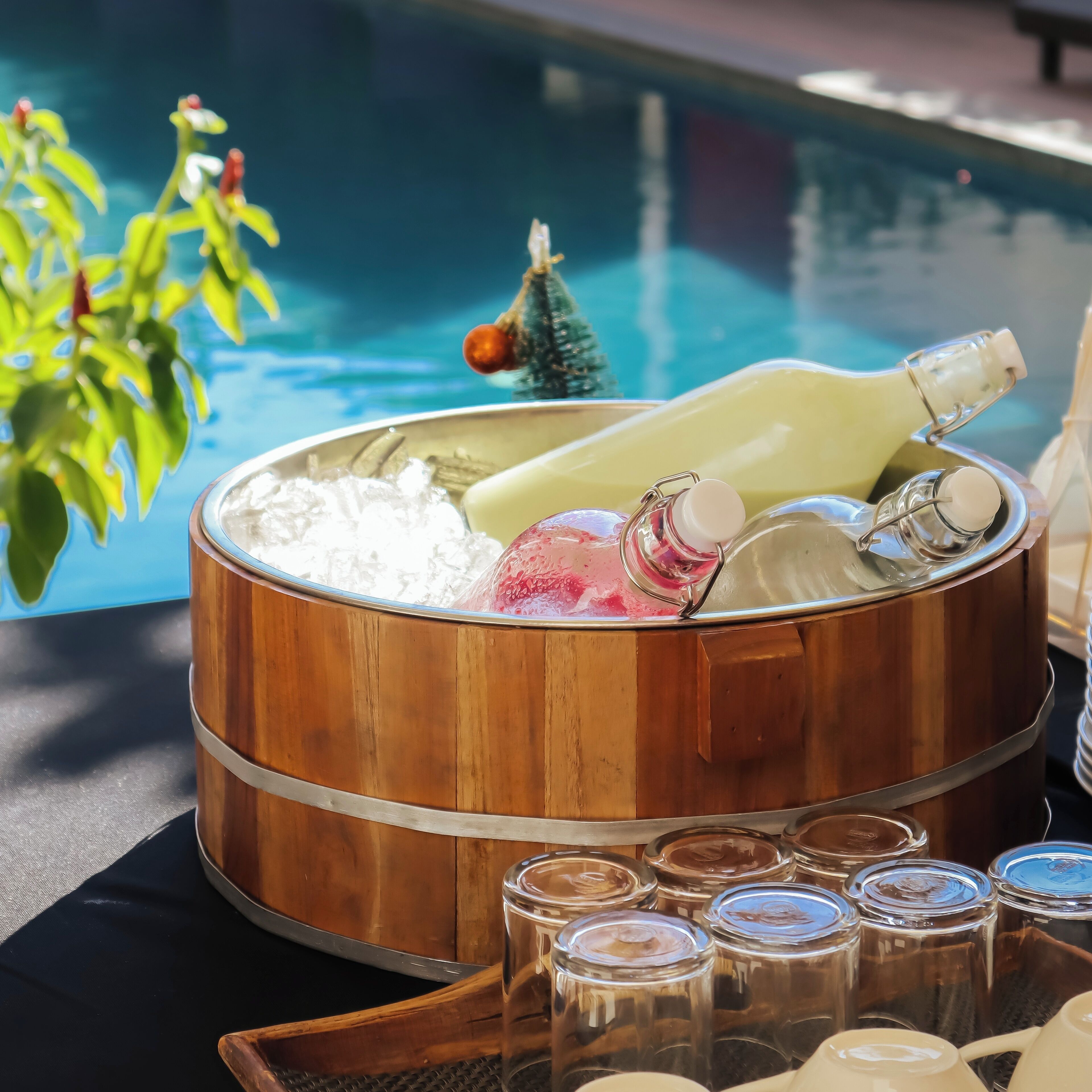 A wooden ice bucket with bottles and glasses, placed near a poolside.