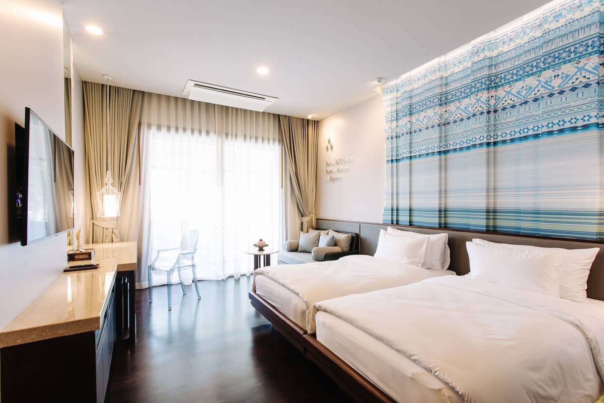 Une chambre d’hôtel avec deux lits, un bureau, une télévision et une grande fenêtre avec des rideaux.