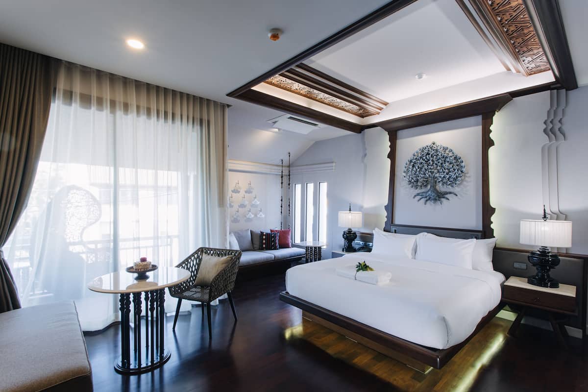 Une chambre d’hôtel avec un grand lit, une petite table ronde, un canapé et un tableau décoratif représentant un arbre accroché au mur.