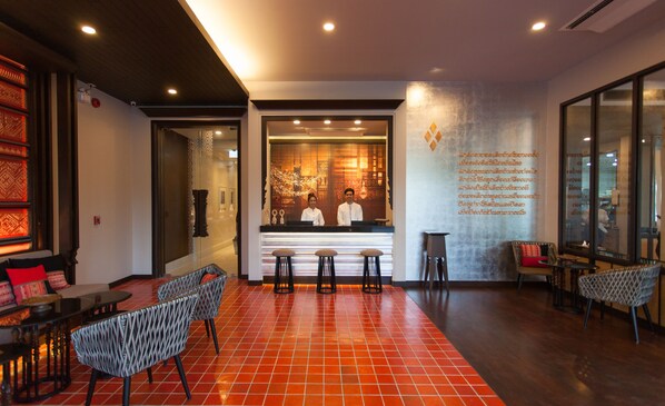 A reception area with a reception desk, three bar stools, and a seating area with patterned chairs and tables.
